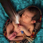 A newborn baby holding a feather.